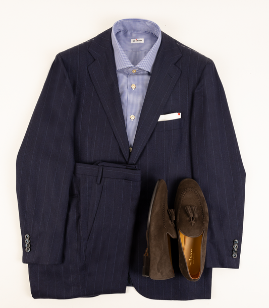 Kiton navy pinstripe suit laid flat with a blue checked shirt, white pocket square and brown suede tassel loafers